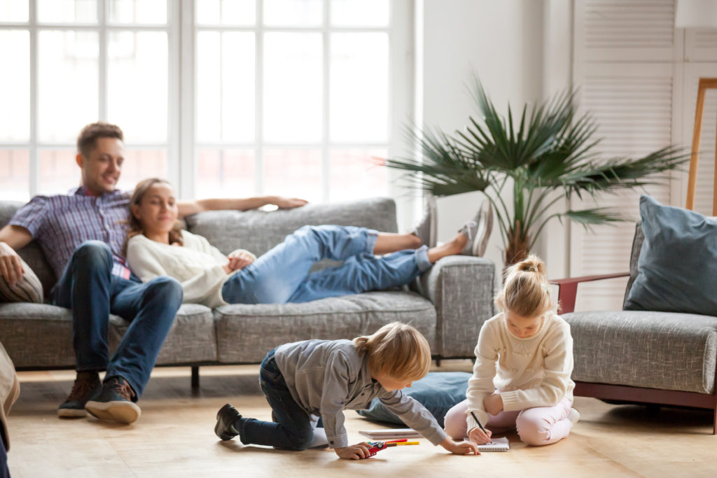 A couple sitting on a sofa, while their kids draw in a notebook with sketches