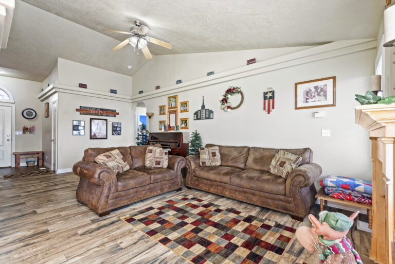 A hall with sofa sets, wall frames, and a ceiling fan