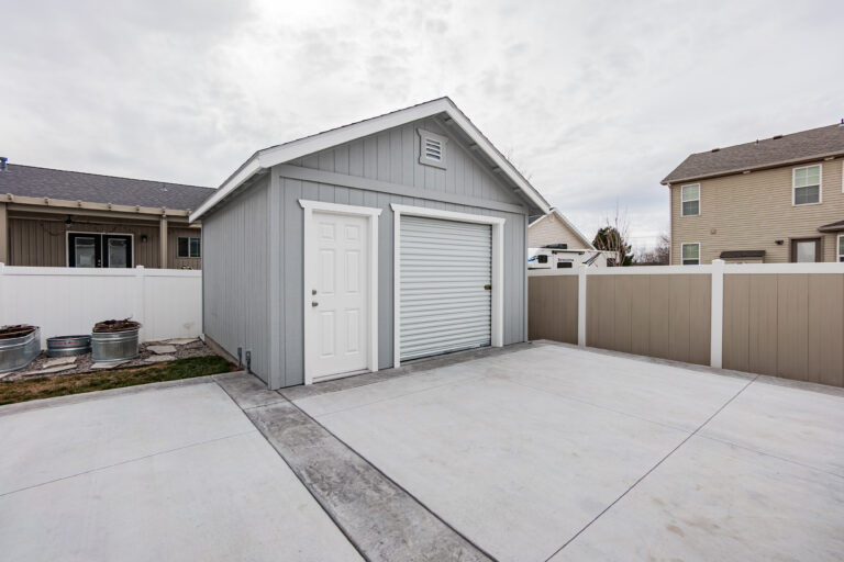 Gray shed with white door and garage, concrete floor, residential area.